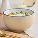 A bowl of Acopa Embers Harvest Tan Matte Stoneware filled with soup on a table.