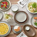 An Acopa Embers Harvest Tan stoneware bowl filled with pasta and peas on a white table with other food and white tableware.