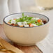 A bowl of food with greens in an Acopa Harvest Tan stoneware bowl.