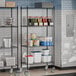 A Steelton black metal wire shelving unit with shelves and casters in a kitchen.
