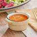 An Acopa Harvest Tan stoneware sauce cup filled with orange sauce on a table.