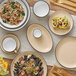 A table with white bowls and plates of food, with an Acopa Harvest Tan stoneware mug on a plate.