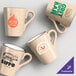 A set of tan matte stoneware mugs with various custom coffee shop logos printed on them.