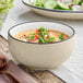 A bowl of soup with a spoon and a salad in it on a white background.