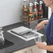 A woman pouring a drink into a glass using a stainless steel container with a sliding lid.