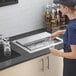 A woman sliding a stainless steel lid onto a Regency drop-in ice bin.