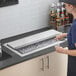 A person holding a glass of wine with a stainless steel Regency sliding lid on a counter in a professional kitchen.