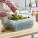 A person in a white apron and gloves using a Vigor translucent plastic food pan to hold greens.