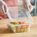 A person wearing a glove securing a Vigor translucent plastic lid on a container of fruit.