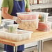 A person holding a Vigor translucent polypropylene food pan filled with green sprouts.