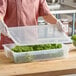 A woman in a pink shirt using a Vigor plastic container with a translucent lid to hold leafy greens.