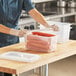 A woman wearing gloves fills a Vigor translucent plastic food pan with carrots on a table.