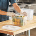 A person wearing gloves putting lemons in a Vigor translucent plastic food container.