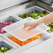 A person using a Vigor translucent polypropylene handled lid on a plastic tray of vegetables at a salad bar.