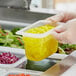 A person in gloves holding a Vigor translucent polypropylene food pan filled with food.