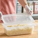 A woman using a Vigor translucent polypropylene lid to seal a plastic container of food.