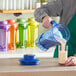 A person pouring a drink from a blue blender jar into a yellow glass.