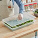 A person holding a Vigor translucent plastic container lid full of green salad.