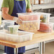 A man holding Vigor translucent plastic food pans filled with food.