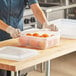 A woman in an apron and gloves using a Vigor translucent plastic container to store oranges.