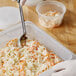 A person holding a Vigor translucent polypropylene food pan filled with coleslaw.