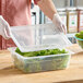 A person in gloves holding a Vigor translucent plastic container with lettuce inside.