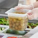 A person in gloves holding a Vigor translucent polypropylene food pan filled with yellow and white food.