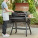 A man in a white apron cooking meat on a Backyard Pro wood-fire pellet grill on a table outdoors.