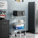 A kitchen with a black Regency microwave shelving kit next to a grey refrigerator.
