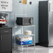 A Regency chrome wire shelf with a black and grey microwave on it.