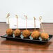 A black rectangular melamine platter with meatballs on sticks on a table.
