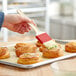 A hand using a Choice natural bristle pastry brush to spread pastry on a tray of pastries.