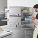 A man in a professional kitchen wearing blue gloves prepares food using a Lincoln countertop impinger oven.