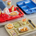 A person holding a red Choice right-handed 7 compartment tray with food in it and a plastic fork and spoon.