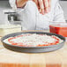 A person sprinkling cheese on a pizza in a pizza parlor.