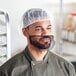 A man in a chef's uniform wearing a white disposable bouffant cap over his hair.