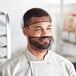 A man in a chef's uniform wearing a brown hairnet over his head.