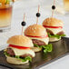 Three hamburgers on a black plate with bamboo ball picks.