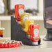 A black 4-section stepped condiment bottle organizer holding yellow and red ketchup bottles on a counter.