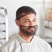 A man in a chef's uniform wearing a black net hairnet over his head.