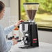 A woman using an Estella Caffe On Demand Espresso Grinder in a professional kitchen.