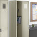 A beige metal locker from Regency Space Solutions with a blue and white striped bag inside.