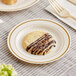 A WNA Comet ivory plastic plate with gold accent bands holding a chocolate cookie with a fork.