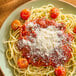 A plate of spaghetti topped with tomato sauce, cherry tomatoes, and a generous sprinkle of grated vegan parmesan cheese.