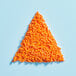 A triangle of Adourne orange sprinkles on a blue surface.