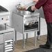 A man cooking food in a wok on a Cooking Performance Group liquid propane wok range.