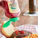 A hand pouring Mama Selita's Jalapeno Ketchup onto a burger.