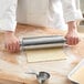 A person using a Choice stainless steel rolling pin to roll out dough on a table.