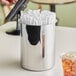 A silver stainless steel container holding straws and utensils.