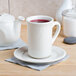 A white Tuxton saucer on a white table with a cup of tea on it.
